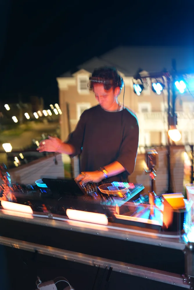 Lane Watt reaching across the decks in a warm-lit performance shot